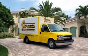 A yellow and white "My Electrician" work truck is parked on the paver driveway of a large house with palm trees.